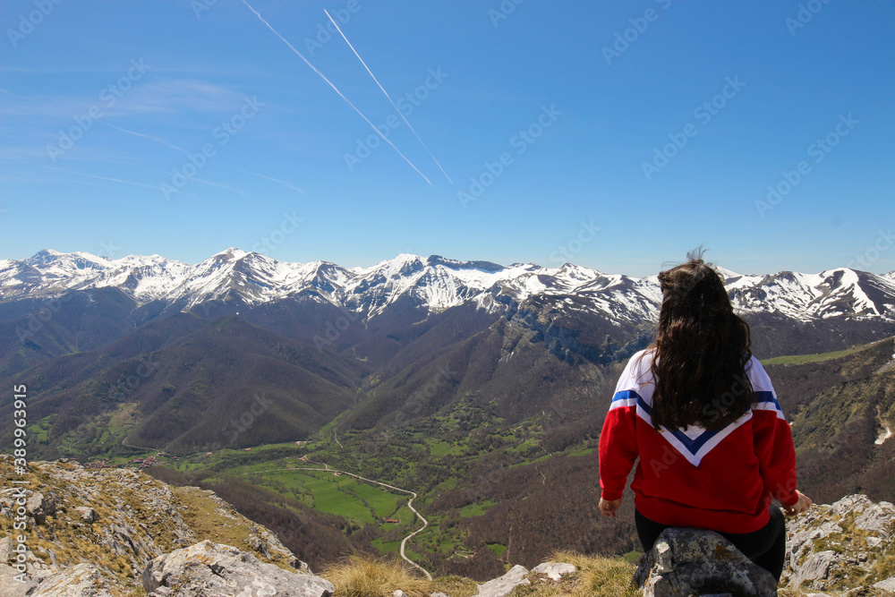 Young girl sitting on a stone at the edge of a cliff with mountains in the background
