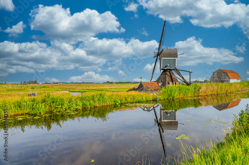 Dutch polder landscape with watermill the Blauwe Wip along the drain canal for the drying of Gerepolder against sky with Dutch clouds sky