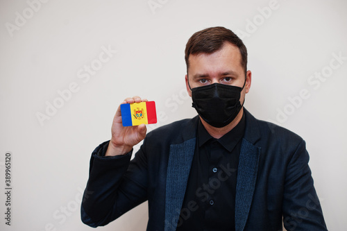 European man wear black formal and protect face mask, hold Moldova flag card isolated on white background. Europe coronavirus Covid country concept.