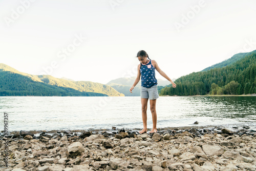 Girl walking along the rocky beach of lake in the mountains