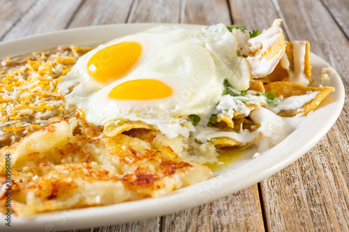A closeup view of a Mexican breakfast plate, featuring chilaquiles, sunny side up eggs, in a restaurant or kitchen setting.
