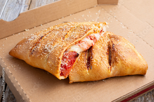 Fotografija A view of a half cut calzone inside a cardboard pizza box.