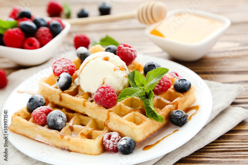 Tasty waffles with fresh berries and ice cream on brown wooden background