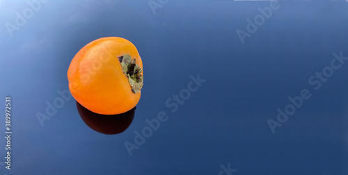 Isolated orange persimmon fruit on blue surface
