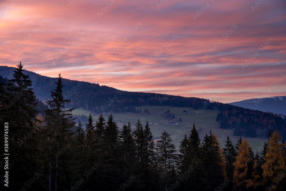 Amazing mountain sunset in Braies, in the Trentino Alto Adige region of Italy. Pink sky at sunset, Dolomite mountains in the background, fall foliage pines and trees. Autumn colors.
