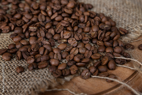 Scattered roasted coffee beans on burlap on a wooden cutting board. Close-up.