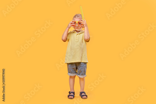 A school-age boy wearing a mask and snorkel. A beautiful boy with blond hair and curly hair. Yellow isolated background.