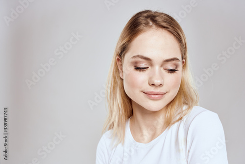 Cheerful blonde woman in white t-shirt cropped view light background © SHOTPRIME STUDIO