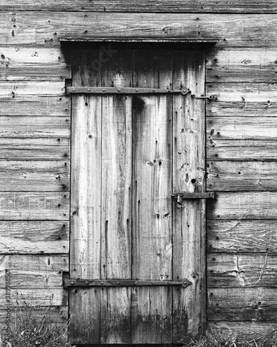 A vintage wood door with iron hinges padlocked shut on a abandoned building. The image was shot on analog film. © Mark