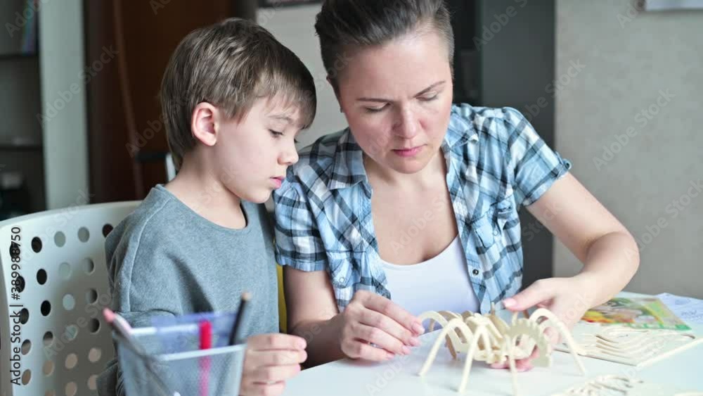 Mom helps her son to make a wooden toy according to the instructions, close-up of hands and toys Mom helps her son to make a wooden toy according to the instructions, close-up of hands and toys