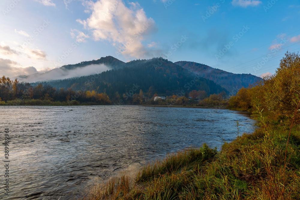 Autumn landscape of a mountain river in the Carpathians. River against the backdrop of the Carpathian mountains covered with fog and autumn forest. Magical landscape of the mountain river Stryi. 
