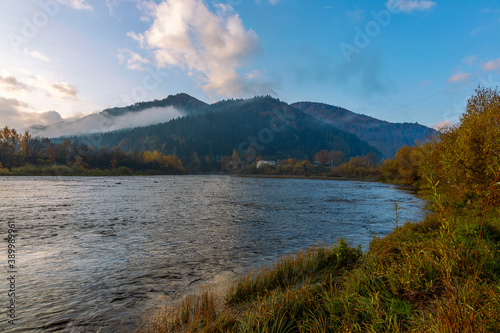 Autumn landscape of a mountain river in the Carpathians. River against the backdrop of the Carpathian mountains covered with fog and autumn forest. Magical landscape of the mountain river Stryi. 