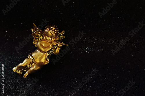 Golden angel on black shiny background, yellow glitter toy, Christmas decoration, place for text
