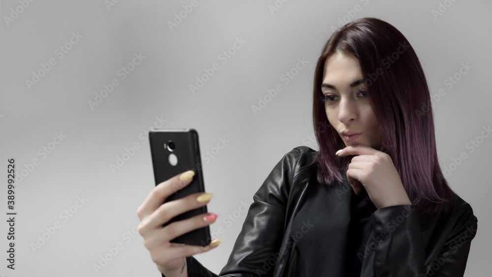 Portrait of pretty young lady who makes selfie posing in front of mobile camera on white background. Caucasian woman does photos on smartphone. Concept of gadgets and social networks in person's life. Portrait of pretty young lady who makes selfie posing in front of mobile camera on white background. Caucasian woman does photos on smartphone. Concept of gadgets and social networks in person's life.