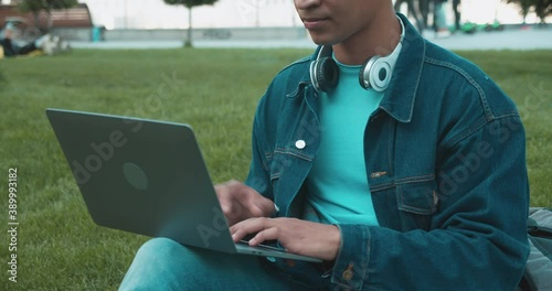 Male college student typing essay on laptop, sitting in park, modern education photo