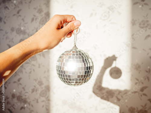 Woman holds sparkling on sun mirror disco ball. Light and shadow. Sunny morning at home. Sun reflections on walls. Symbol of music parties or holidays.
