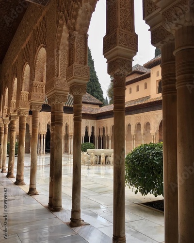 Side view of the court of the Lions at the with a view of the fountain through a row of arched columns at the Alhambra palace and fortress complex - Granada, Spain