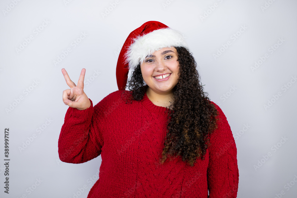 Young beautiful woman wearing a Santa hat over white background showing and pointing up with fingers number two while smiling confident and happy Young beautiful woman wearing a Santa hat over white background showing and pointing up with fingers number two while smiling confident and happy