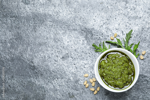 Bowl of tasty arugula pesto and ingredients on grey table, flat lay. Space for text