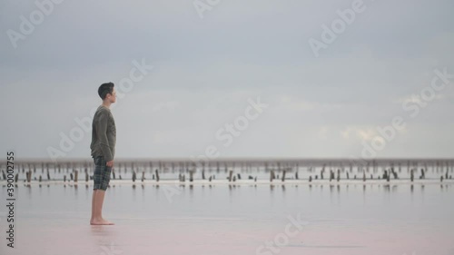 Encouraged boy standing on a sea coast and looking far away in windy weather