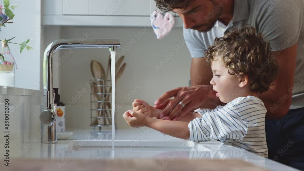 Father helping young son to wash hands in kitchen sink during health pandemic - shot in slow motion
