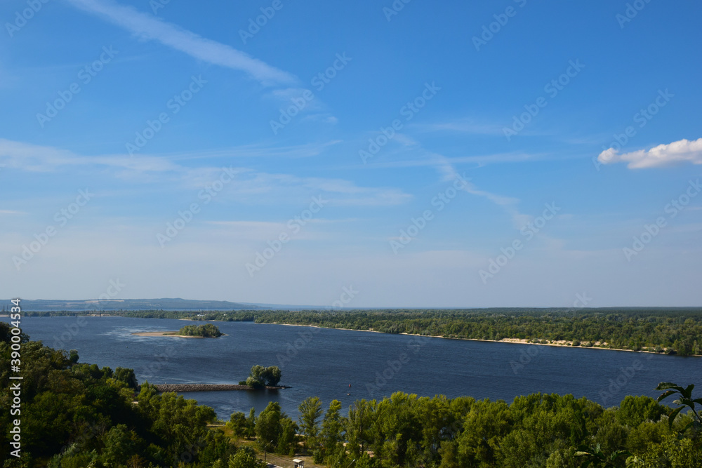 Summer big river with forests growing on the sides against the blue sky. There are islands in the center of the river.