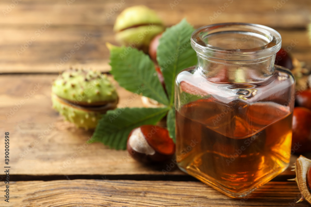 Chestnuts and jar of essential oil on wooden table. Space for text