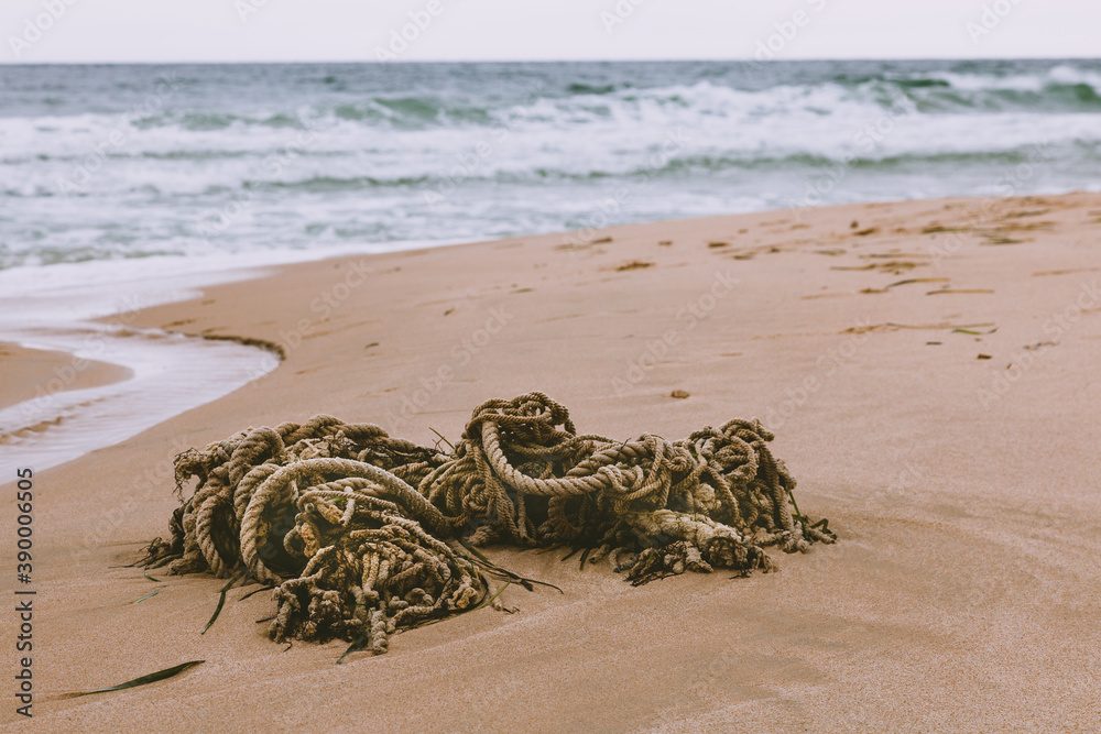 Obraz premium The old rope is lying on the sand on the beach against the background of the sea and waves.