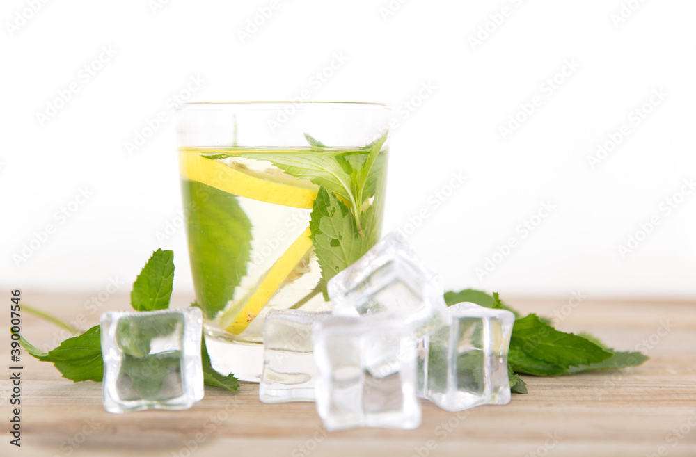 Fototapeta premium Looking down on a glass of iced lemon mint water and fresh mint leaves and scattered ice cubes on the table