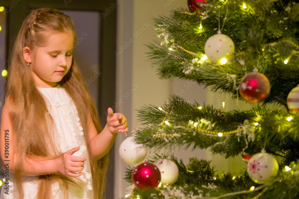 Little girl decorates a Christmas tree. New Year concept, family holidays.