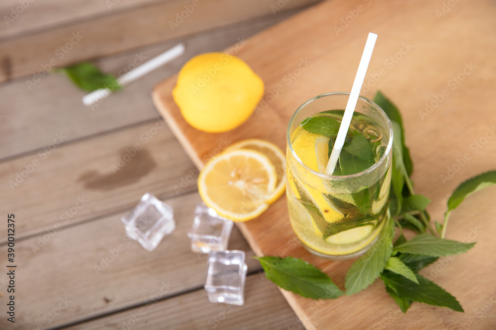 Fototapeta premium A glass of lemon cucumber water and fresh lemon fruit, ice cubes and mint leaves on a cutting board