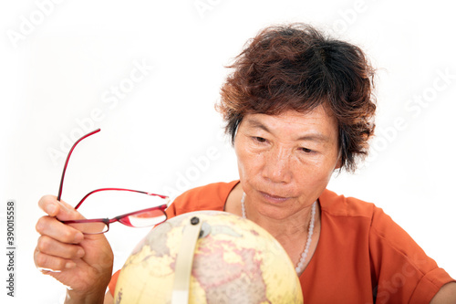 Фотография An old Chinese lady carefully looking at the globe in front of a white backgroun