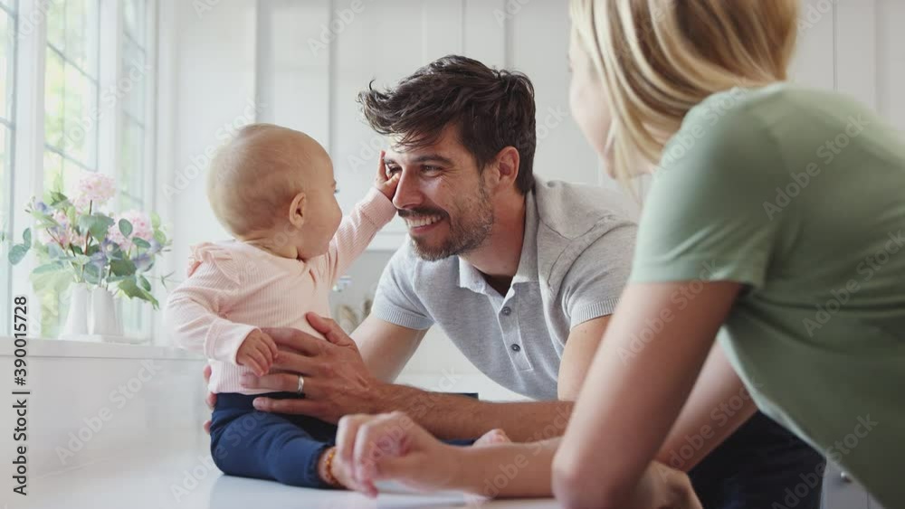 Family with baby daughter having fun playing game sitting in kitchen together - shot in slow motion Family with baby daughter having fun playing game sitting in kitchen together - shot in slow motion