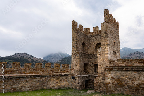 Tower and wall of Genoese fortress of 14th century in the Sudak bay on the Peninsula of Crimea on the background of mountains and cloudy sky