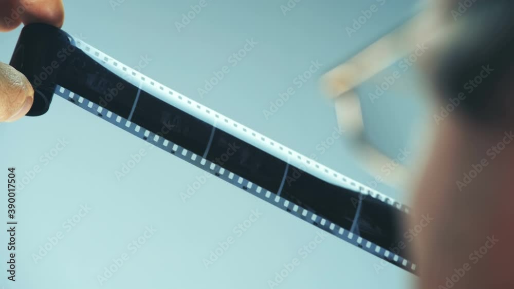 A photographer examines an old black and white negative camera roll against a light background and searches for the desired frame