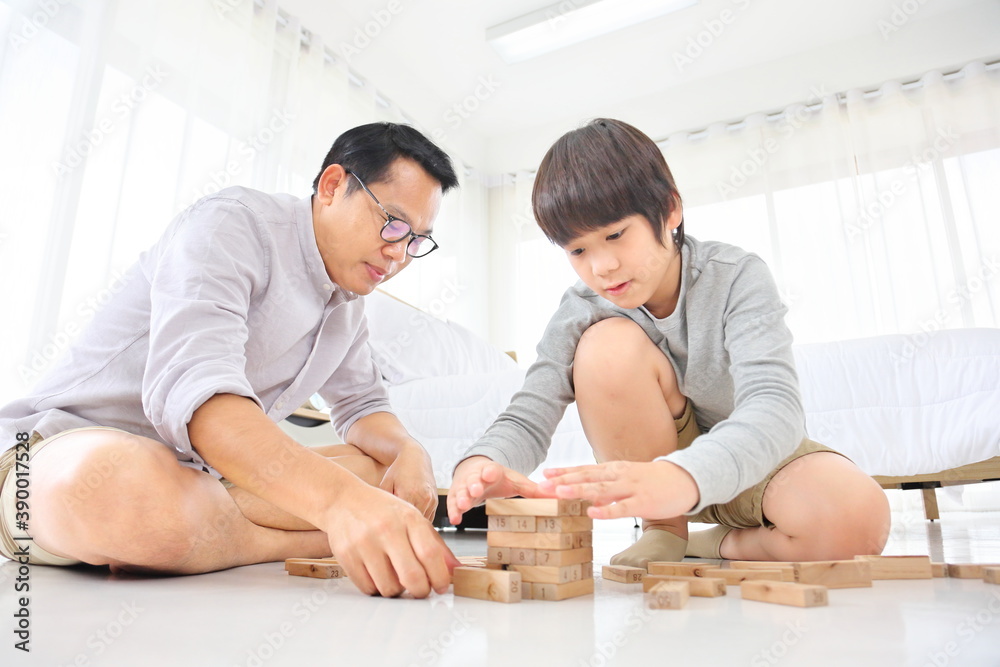 Asian father and son concentrate on playing wooden block together at home for edutainment concept