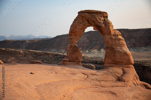 View of the delicate arch in arches national park at sunset. The sun can be seen and the land around it is lit up from the sunset. 
