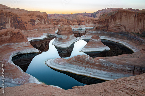 View of Reflection canyon near escalante, utah. The orange canyon includes two large rock formations surounded by reflective winding water from a river. 