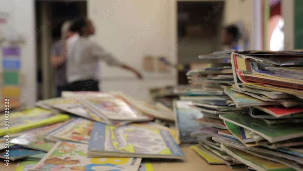 Teachers Talk in Empty Classroom in Distance, Pile of Books on Desk in Foreground, Depth Teachers Talk in Empty Classroom in Distance, Pile of Books on Desk in Foreground, Depth