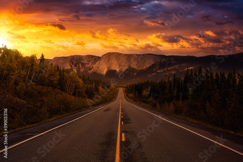 View of Scenic Road surrounded by Trees and Rocky Mountains on a Cloudy Fall Season in Canadian Nature. Colorful Sunset Artistic Render. Taken near Whitehorse  Yukon  Canada.