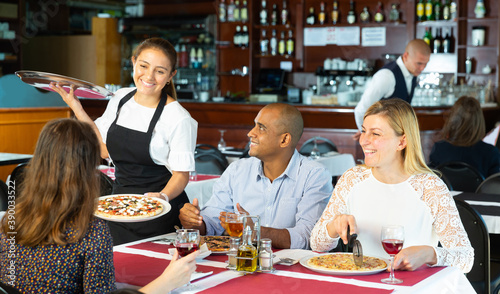 Hospitable latin american waitress bringing ordered pizzas to guests of cozy pizzeria