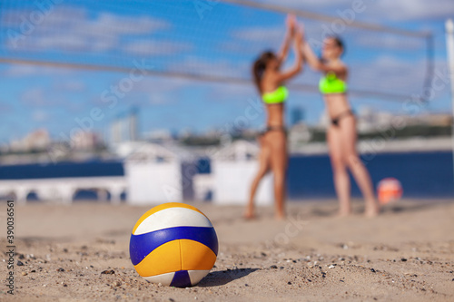 Close up of a ball on the sand on a blurry background of two happy girls enjoying a victory in beach volleyball