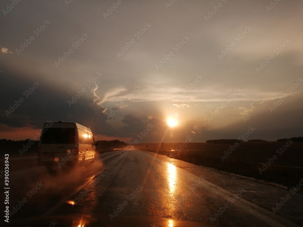 Road after thunderstorm in splashes of rain, car at high speed in sunset