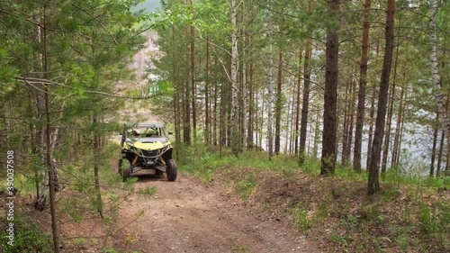 Tracking shot of unrecognizable people in helmets driving yellow ATV uphill along narrow forest road photo