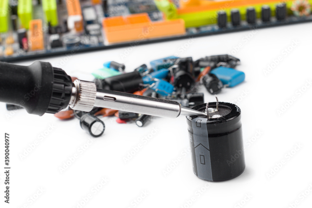 soldering iron on the background of a computer Board and capacitors in soft focus. soldering iron on the background of a computer Board and capacitors in soft focus.