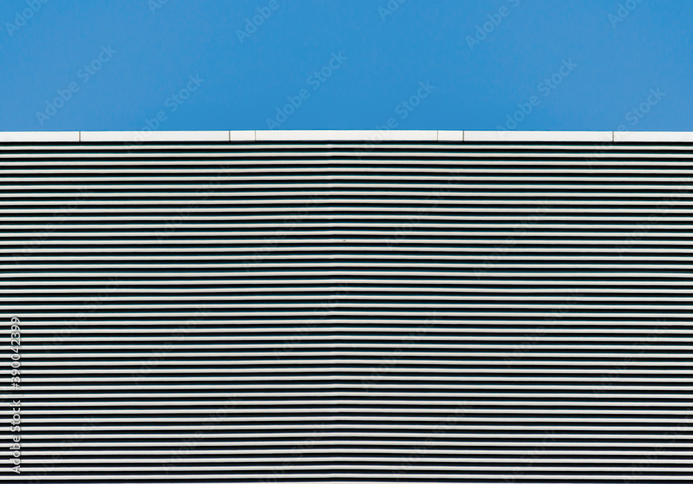 Obraz premium striped wall of a gray tall building against a blue clear sky