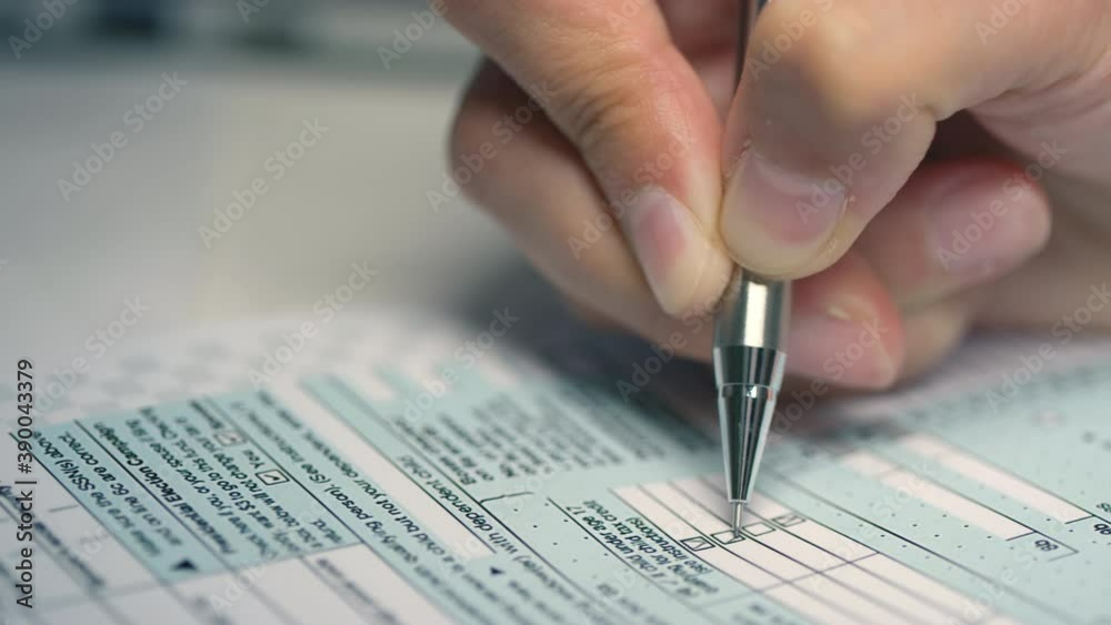 Closeup of unrecognizable female hand holding pen filling out printed tax declaration form ticking boxes