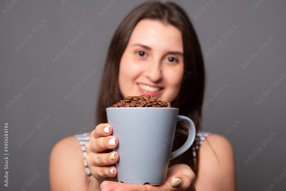 Portrait of a young woman holding a mug with coffee beans. Portrait of a young woman holding a mug with coffee beans.