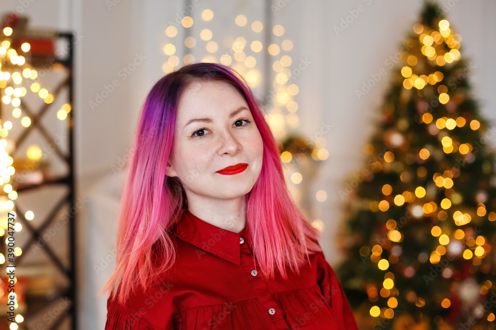 A woman with pink hair and a red dress near the fireplace in a beautiful home interior and smiles while looking at the camera. Happy lady. Home decor design. Luxury house of December A woman with pink hair and a red dress near the fireplace in a beautiful home interior and smiles while looking at the camera. Happy lady. Home decor design. Luxury house of December