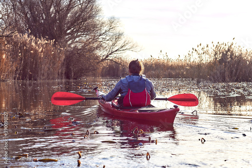 Back view on man paddle in red kayak among bulrush on lake at autumn season